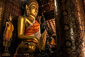 Wat Xieng Thong temple in Luang Prabang, Laos.  The main Buddha of the sim sits on a platform, surrounded by smaller statues, candles, and offerings. 